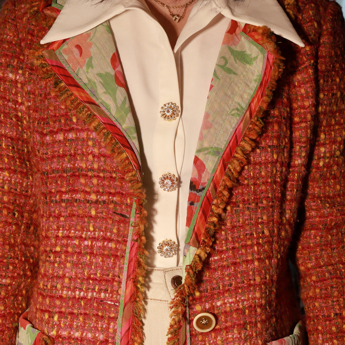 A close-up of a fashion outfit featuring a red and orange tweed jacket with fringed edges, layered over a cream-colored shirt with decorative Bellis Gold Plated Button Cover