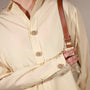 A close-up of a person wearing a cream-colored long-sleeve button-up shirt with decorative Bellis clip-on button cover and holding a brown leather shoulder bag strap.