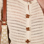Close-up of a cream open-knit cardigan with retro dahlia button covers from button vena, worn by a model with a patterned shoulder bag visible on the left.