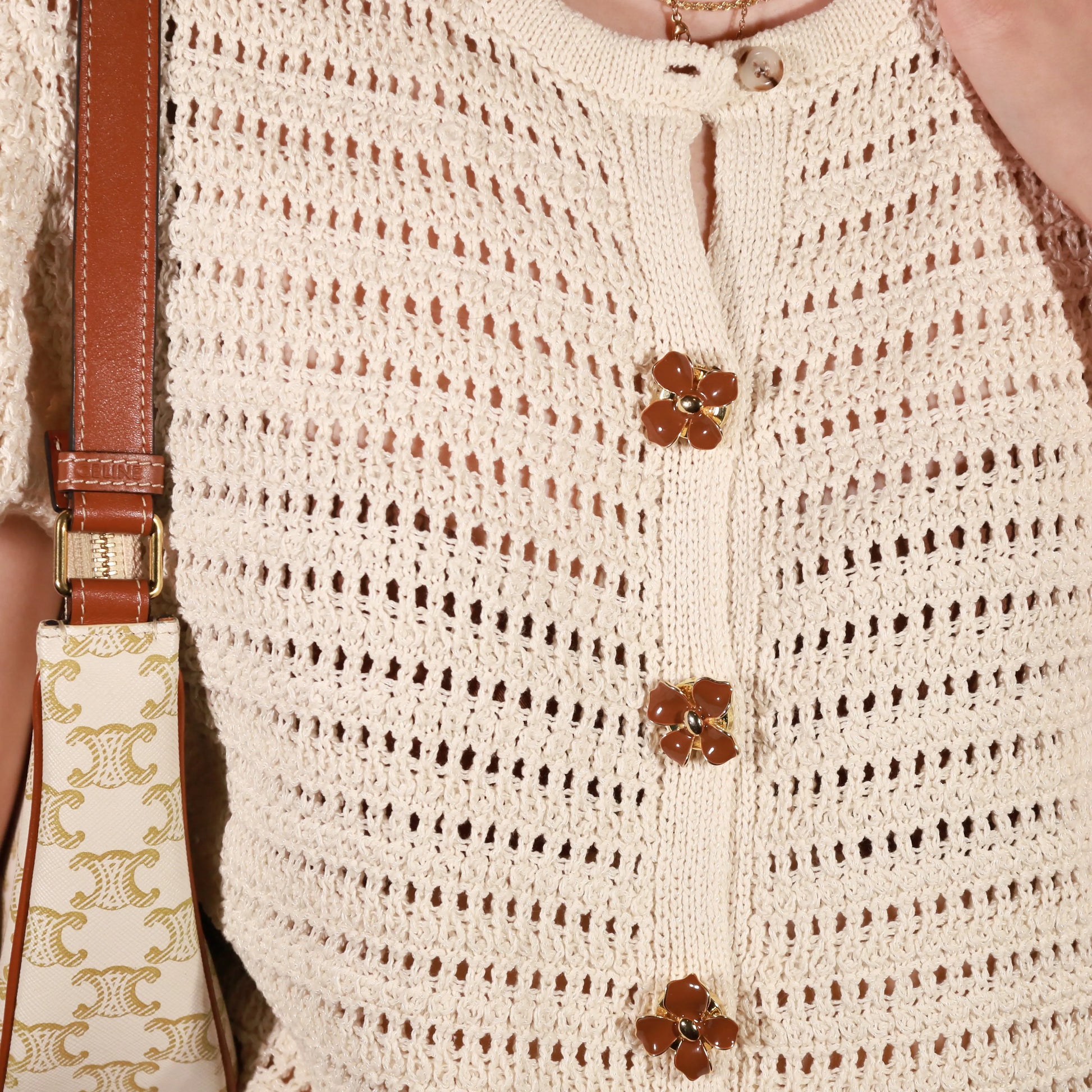 Close-up of a cream open-knit cardigan with retro dahlia button covers from button vena, worn by a model with a patterned shoulder bag visible on the left.