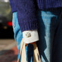 A close-up lifestyle shot of a person wearing a dark navy knit sweater, blue jeans, and holding a beige tote bag. The person is wearing the iris silver plated button covers.