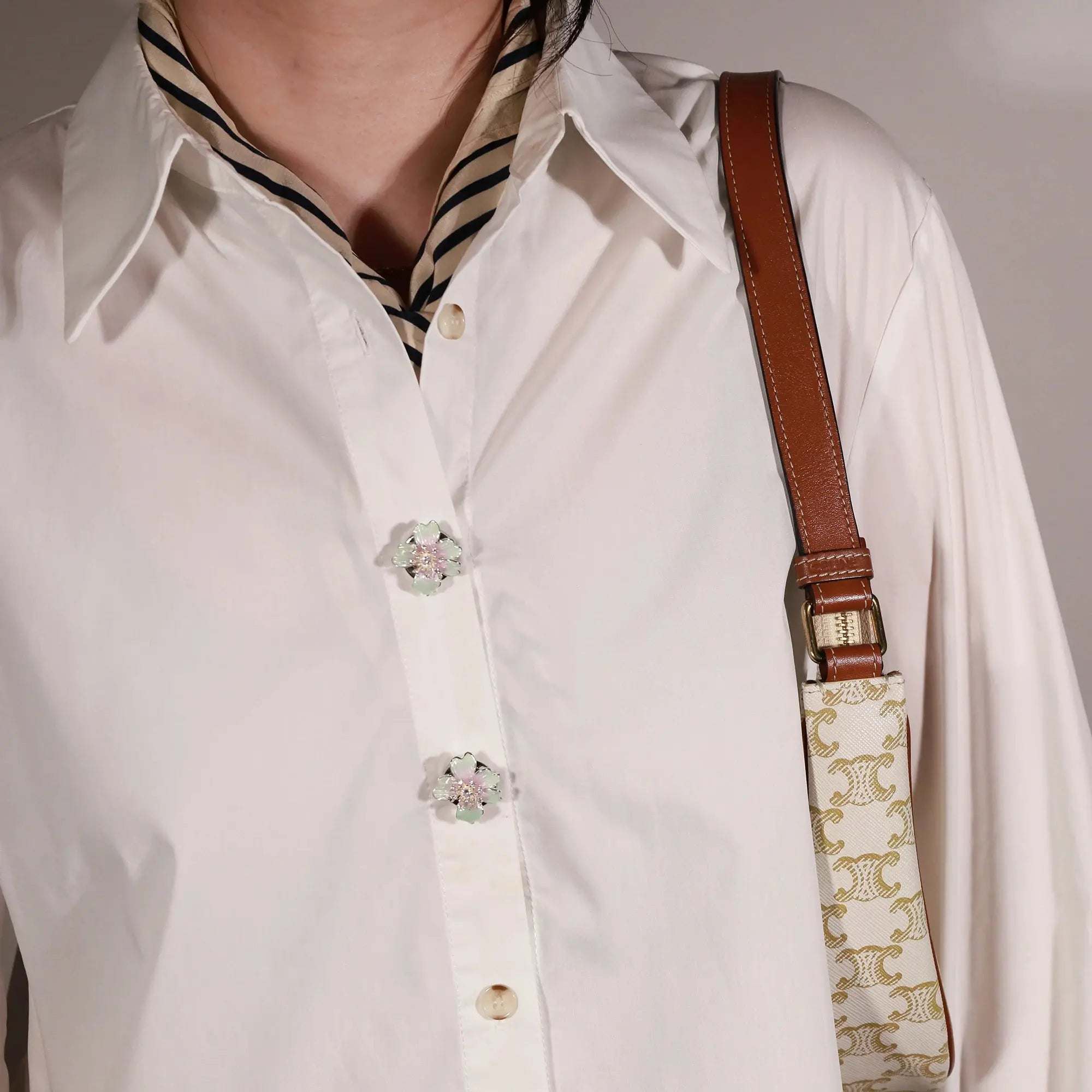 A close-up of a person wearing a white button-up shirt with decorative floral button cover, the iris from button vena